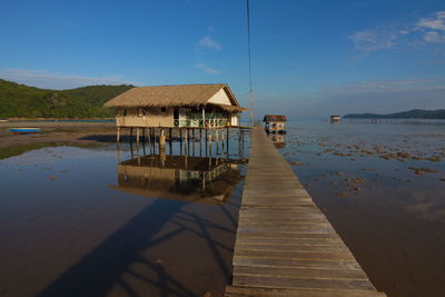 Pier on lake by houses against sky