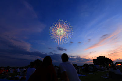 People watching firework display against sky during sunset