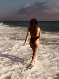 Rear view of woman walking at beach against sky