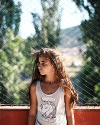 Close-up of girl looking away while standing against chainlink fence