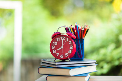 Close-up of colored pencils in desk organizer with books and alarm clock at home