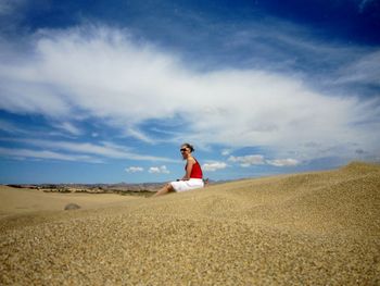 Side view of woman sitting on sand at beach against sky