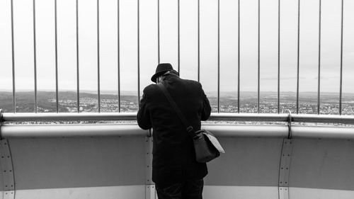 Rear view of man standing by railing against sky