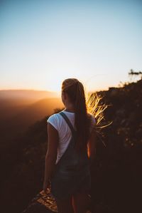 Rear view of woman standing on mountain against clear sky