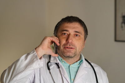 Portrait of mature doctor using phone against wall