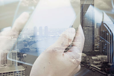 Digital composite image of hands holding smart phone against cityscape