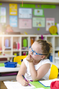 Thoughtful girl writing in paper at kindergarten