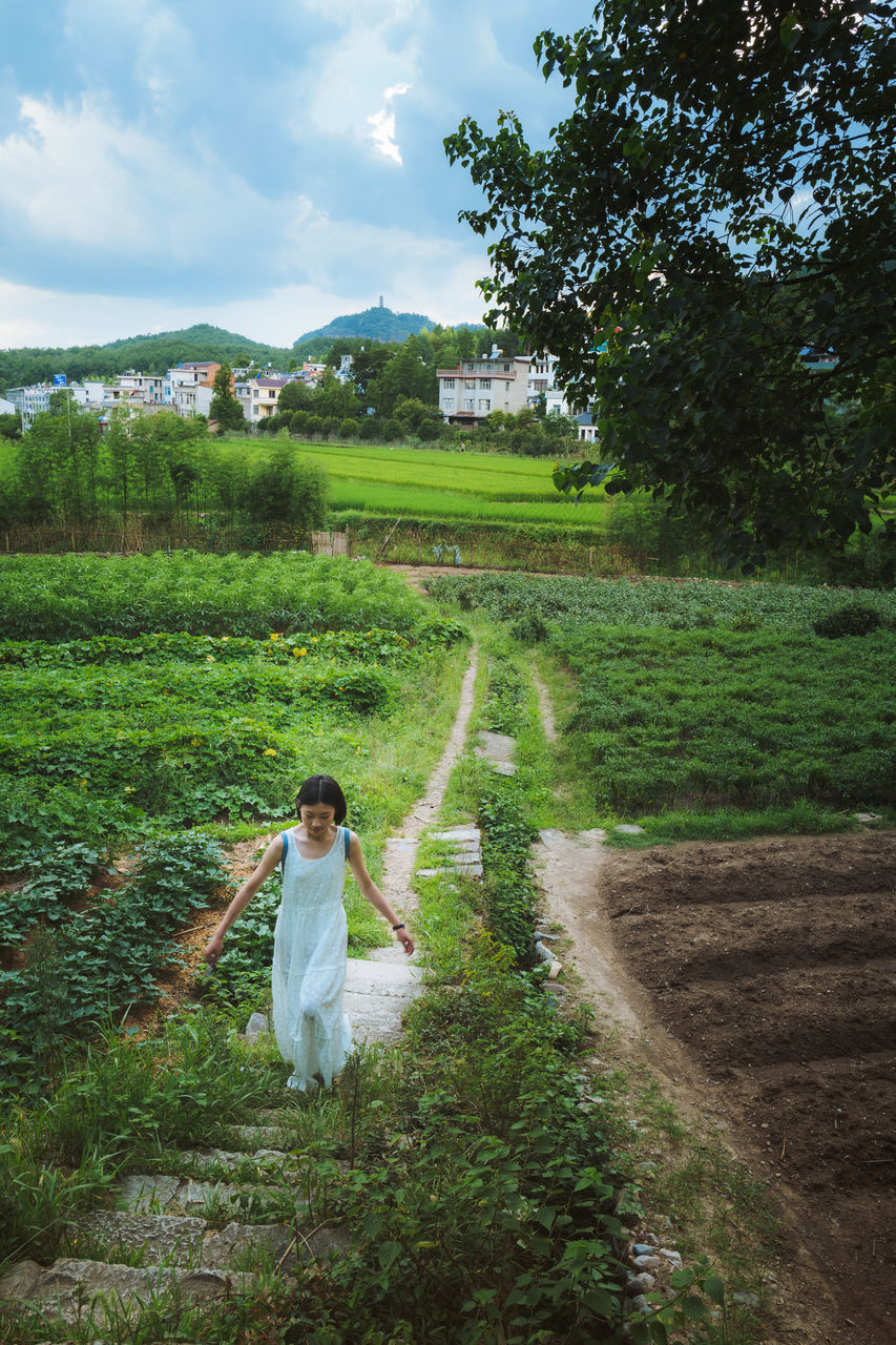 WOMAN STANDING ON FIELD AGAINST TREES AND PLANTS