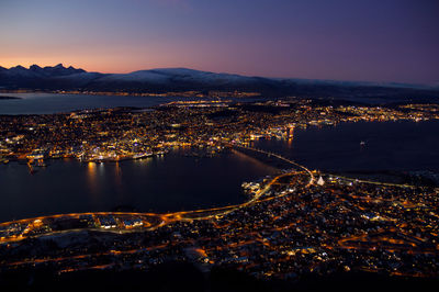 Aerial view of illuminated city by sea against sky at sunset