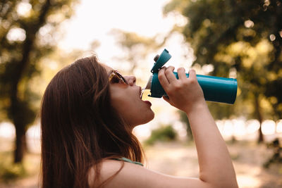 Portrait of woman holding sunglasses against trees