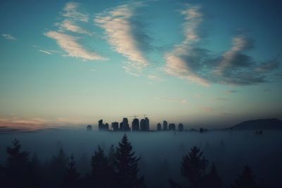 Silhouette of city against cloudy sky during sunset