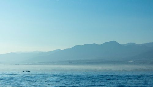 Scenic view of sea and mountains against clear blue sky