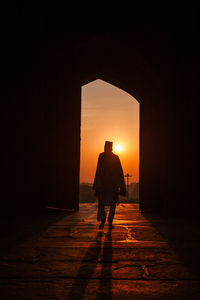 Rear view of silhouette man walking in corridor during sunset