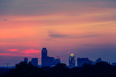 Silhouette trees against cityscape during dusk