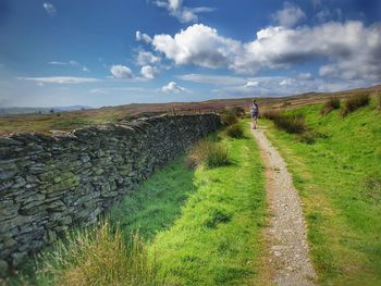 Scenic view of hiking trail. dry stone wall with blue sky and white clouds. walker in distance.