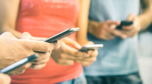 Midsection of friends using mobile phones while standing outdoors