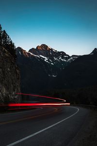 Light trails on road against clear blue sky