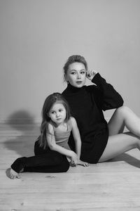 Mother in a black sweater hugs her five-year-old daughter sitting on a chair in the room in front