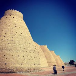 Tourists on stone wall against clear sky