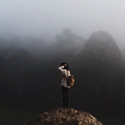 Rear view of woman standing on rock during foggy weather
