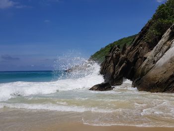 Sea waves splashing on rocks against sky