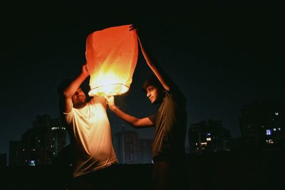 Friends holding illuminated paper lantern at night