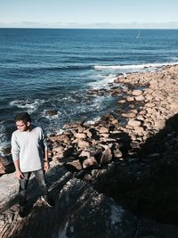 High angle view of young man standing on rock by sea against sky