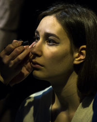 Cropped hands applying eyeliner to woman