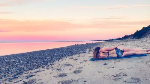 Woman lying on beach against sky during sunset