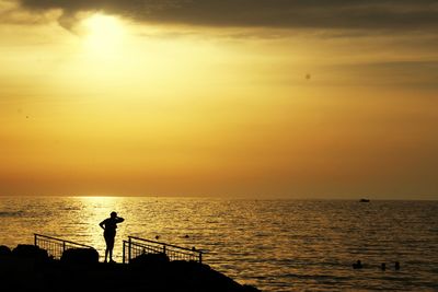 Silhouette man in sea against sunset sky