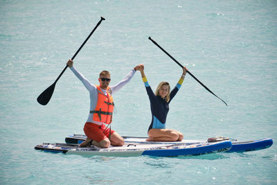 Young man dressed in swimsuit and lifevest and young woman holding hands on stand up paddle board