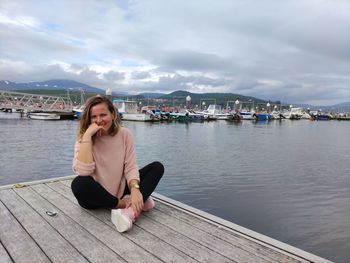 Portrait of woman sitting on pier against sky