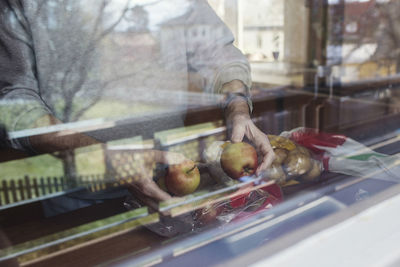 Midsection of senior man holding apples at kitchen counter seen through glass window