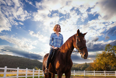 Woman riding horse in ranch against sky