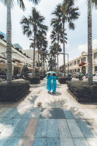 Rear view of people walking on footpath by palm trees