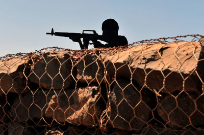Silhouette army soldier aiming gun by rock formations