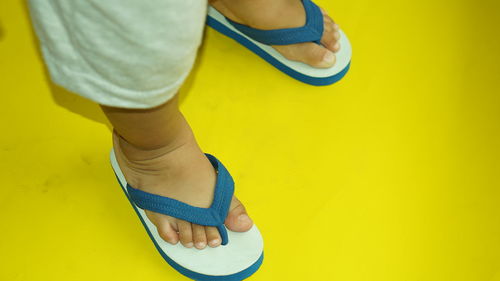 Low section of baby boy wearing flip-flops while standing over yellow background