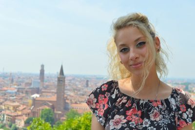 Portrait of beautiful young woman standing against sky in city