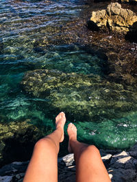 Low section of woman sitting on rock at sea