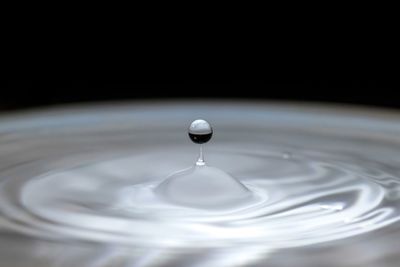 Close-up of drop splashing on water against black background