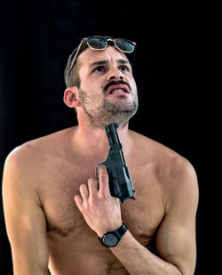 Shirtless man attempting suicide with gun against black background