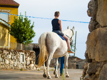 Boy riding horse on road against sky