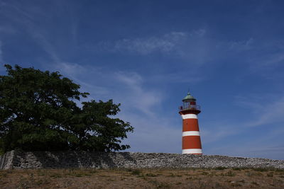 Lighthouse amidst trees and buildings against sky