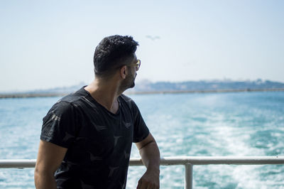 Young man standing by railing against sea