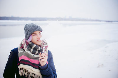 Young woman wearing warm clothing smoking electronic cigarette during winter