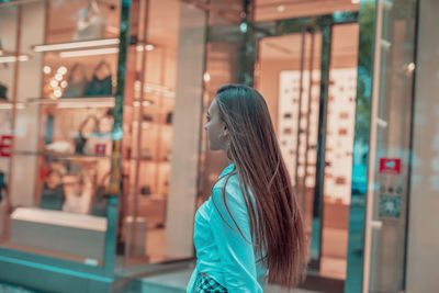 Side view of woman standing on footpath by store window