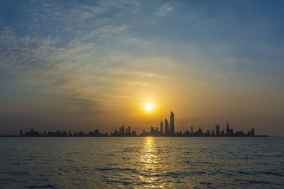 Silhouette buildings by sea against sky during sunset