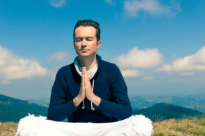 Young man sitting on mountain against sky