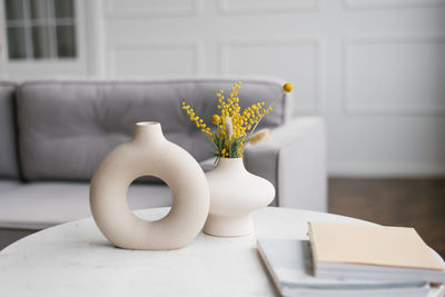 Modern ceramic vases with bouquets of mimosa flowers on a coffee table in the living room