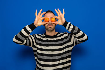 Man covering eyes with oranges against blue background